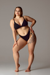 Full length portrait of young chubby woman posing in lingerie against grey studio background....