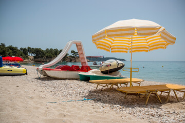 Two sunbeds with mattresses stand on the sand in the shade of a sun umbrella.