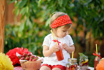 Lemonade Stand. Adorable little girl trying to sell lemonade. strawberry lemonade with ice and mint as summer refreshing drink in jars. Cold soft drinks with fruit. Child drinking lemonade in jar