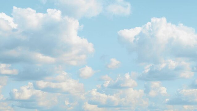 Blue sky covered with slowly moving white clouds. A bright landscape with cumulus clouds floating from left to right.