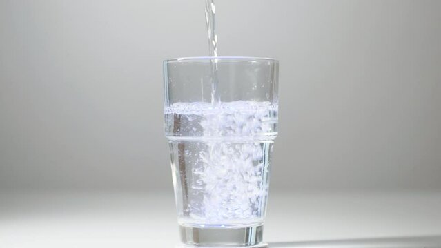 Pouring impure drinking water into a glass with blue light. Close-up of pouring not fresh, contaminated drinking water into a glass on a white background. Drink concept, healthy