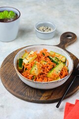 Asian style pickled carrot and fresh cucumber salad sprinkled with sesame seeds in a gray ceramic bowl on a gray concrete background. Salad recipes. Vegan recipes.