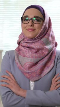 Portrait of professional young muslim business woman looking at camera laughing wearing traditional headscarf. Vertical video for smartphone screen, for target social media platforms and web browsers