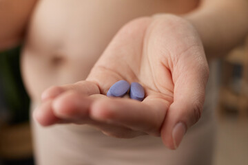 Closeup of woman hand holding pills or vitamins for pregnant females showing her bare belly...