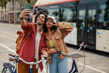 A happy couple is standing on street with bikes and taking selfies.