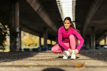 A fit sportswoman crouching in urban exterior and tying shoelace.