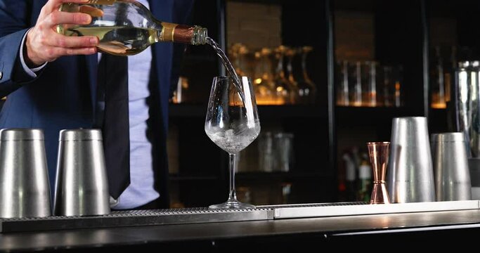 Close up of a barman pouring white wine in a glass. Professional bartender pouring champagne in a glass. Close up of a bartender hand pouring Italian prosecco white wine into glass at a bar counter.