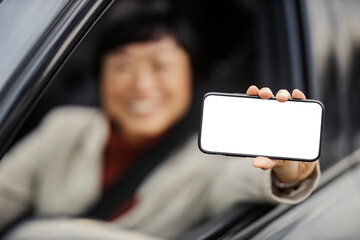 Close up of an asian businesswoman showing a mobile phone at the camera while sitting in a car.