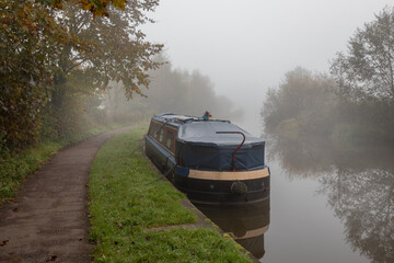 A narrow boat is moored up along side the towpath. Looking into the distance is an early morning mist