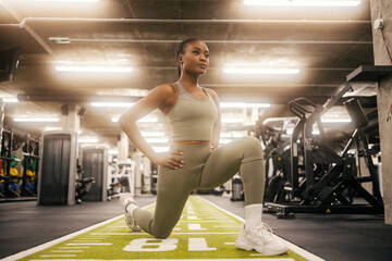 A sporty black woman is doing lunges and working out her gluts and legs at gym.