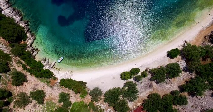 Orbiting drone shot of the stunning crystal clear waters and white pebbles of Foki Beach, located just a few kilometers from the world famous Fiskardo village, in Greece.