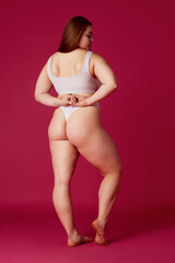 Full length rear-view portrait of young overweight woman posing in lingerie, black bikini showing...