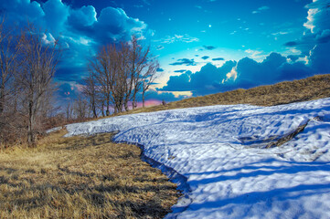 Yellow fields contrast with white snow. The trees stand bare, protecting from the cold. A mixture...