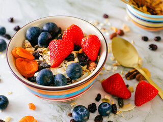 A colorful bowl of oatmeal with strawberries, blueberries, dried fruits and nuts.