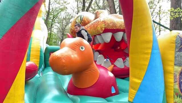 Child jumping on colorful playground trampoline. Kids jump in inflatable bounce castle on kindergarten birthday party Activity and play center for young child. Little boy playing outdoors in summer.