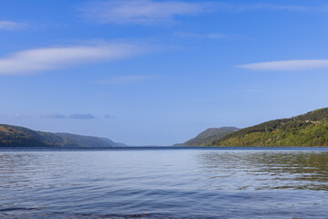 Fototapeta na wymiar The calm waters of Loch Ness stretch towards the horizon, framed by verdant, forested hills under a vast sky. This iconic Scottish lake invites contemplation and exploration