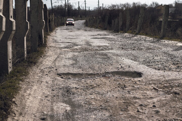 Awful road in the countryside full of holes and potholes and a car moving along this road © Mikhail