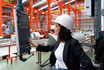 A woman in black suit and a hardhat is carefully observing a machinery monitor in a bustling...