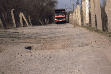 A pothole in the road and a truck  in the background that is moving towards this pothole