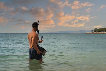 Snorkeling at sea. A man in swimming trunks with fins, a snorkel mask and an action camera in the...