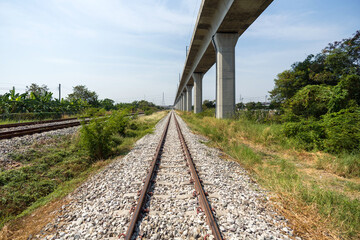 A traditional railway track lined with gravel ballast running parallel to a modern elevated rail....