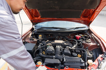 A mechanic in uniform and protective glove looks at a sport car's engine to fix it. Working...