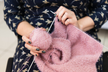 Hands of a woman knitting with pink wool, one hand holds a ball of thread for knitting