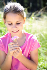 Smile, kid and girl with flower in nature for summer vacation, development and relax in grass field. Garden, happy and child with plant for sunshine, holiday and adventure in green environment