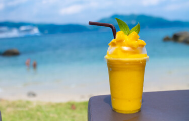 Smoothie made from fresh mango fruits against the backdrop of a seascape. Fruit and yoghurt ice cream decorated with leaves. Glass of tropical dessert close-up.