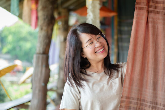 Asian mid adult woman holds woven fabric which was decorated on ceiling of local cafe for tourist watching and taking photos, soft focus, happiness of humans concept.