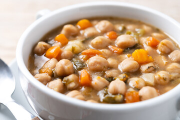 Chickpeas soup with vegetables in bowl on wooden table. Close up