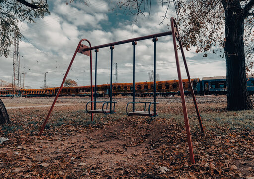 empty swings on an empty playground without people against the background of burnt trains in Ukraine