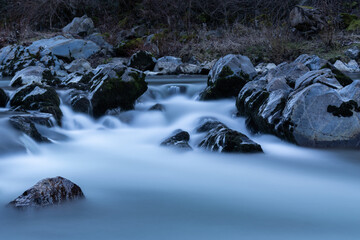 Mountain stream during blue hour with silky water, rapid creek flow around wet rocks in long exposure