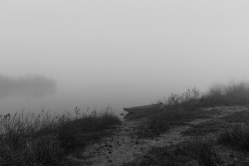 Muddy path leads to moored boat in fog, calm foggy evening near river, nautical vessel