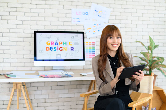 Asian female artist drawing something on graphic tablet. graphic designer working at office. Looking at camera.