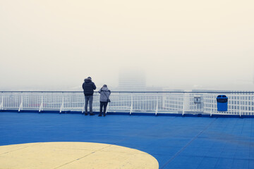 Rear view of passengers on a ferry deck observe mist enveloping the surroundings