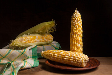Clay plate with two cobs sweet corn on wooden background..
