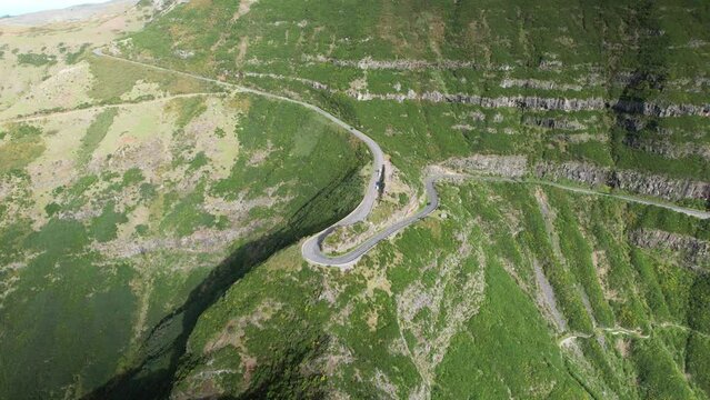 Car drive sharp hairpin turn in steep Madeira mountain hillside; drone parallax