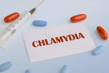 Medical concept. Word Chlamydia. on a white business card on a blue background next to a syringe, pills, vitamins