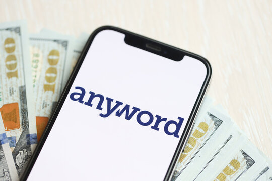 KYIV, UKRAINE - MARCH 17, 2024 Anyword logo on iPhone display screen with many hundred dollar bills. Artificial Intelligence engine