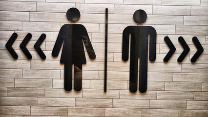 Male and Female Restroom Symbols on a Wooden Wall With Directional Arrows. Gender-specific bathroom signs on wood surface - obrazy, fototapety, plakaty