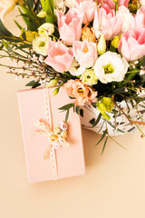 Beautiful bouquet of rose and tulips flowers and pink gift box on beige pastel background. Floral arrangement. Gift for holiday, birthday, Wedding, Mother's Day, Valentine's day, Women's Day.