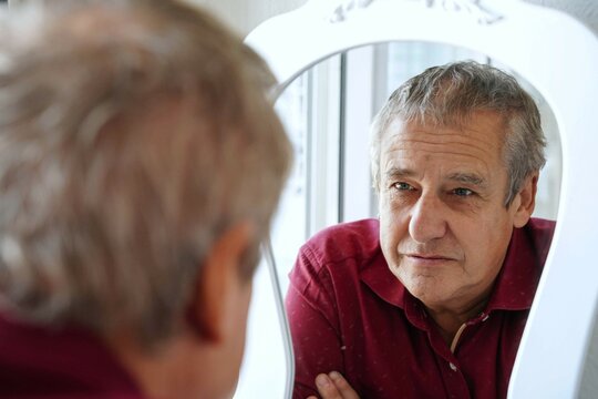 Sad mature man looking at his reflection in a mirror. Mental health concept