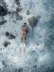 Woman free diver swimming with Sting ray fish in blue ocean.