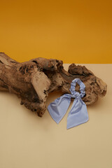 Close-up shot of a satin violet bow scrunchie. Women's scrunchie hair band decorated with bow is lying on a decorative tree root on orange background. Top view.