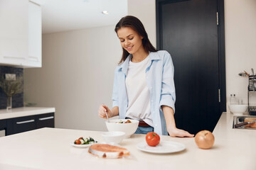 Woman preparing healthy meal in kitchen with bowl of food and plate of vegetables