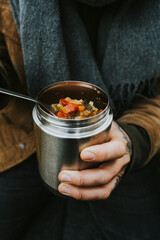 Person holding cup with soup and vegetables in an outdoor forest