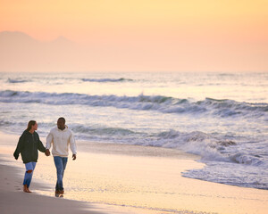 Casually Dressed Loving Young Couple Walking Along Beach Shoreline Holding Hands At Sunrise