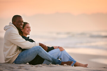 Casually Dressed Loving Young Couple Sitting On Beach Shoreline Hugging At Sunrise