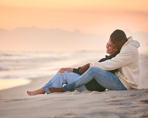 Fototapeta na wymiar Casually Dressed Loving Young Couple Sitting On Beach Shoreline Hugging At Sunrise